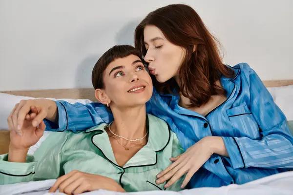 A young lesbian couple relaxes in bed, wearing pajamas, sharing a tender moment. — Stock Photo