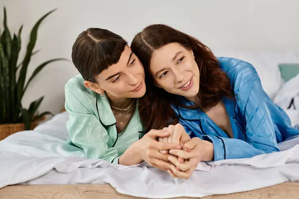 Two women in pajamas lay in bed, holding hands and gazing at each other with affection. — Stock Photo