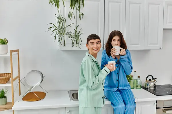 A young lesbian couple enjoys a quiet morning together, sharing coffee and smiles in their pajamas. — Stock Photo