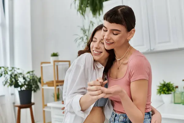 A young lesbian couple shares a tender embrace in their kitchen, filled with warmth and love. — Stock Photo