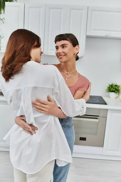 Two women hug in their kitchen, their eyes locked in a tender moment of love and affection. — Stock Photo