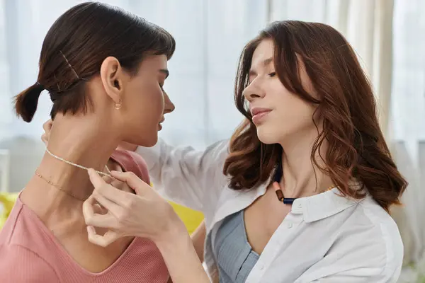 A young lesbian couple shares a tender moment together, with one woman carefully placing a necklace on the others neck. — Stock Photo