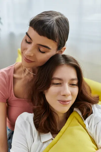 A young lesbian couple shares a tender moment, snuggling on a couch as the morning sun streams in. — Stock Photo