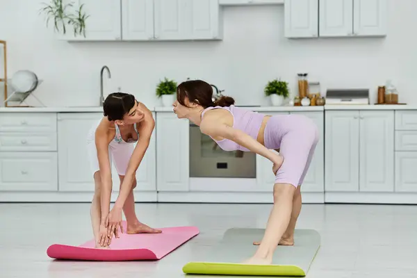 Two young women in athletic wear practice yoga together in a modern kitchen. — Stock Photo