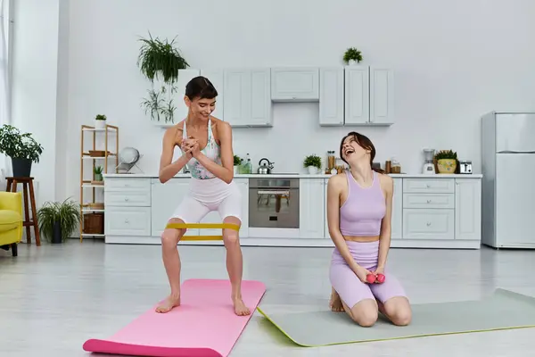 Two women in sportswear laugh while exercising together in their apartment. — Stock Photo
