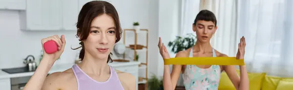 Una coppia lesbica si allena nel suo appartamento - uno con un manubrio rosa e l'altro con una fascia di resistenza gialla — Foto stock
