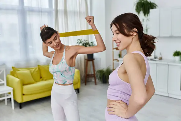 A young lesbian couple works out together in their modern apartment, one woman using a resistance band. — Stock Photo