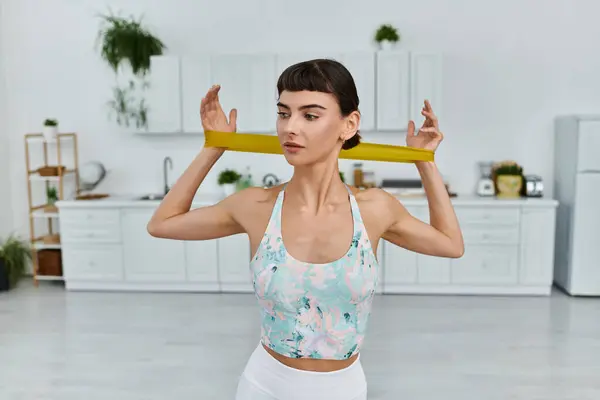 A young woman in sportswear uses a resistance band to work out in a modern kitchen. — Stock Photo