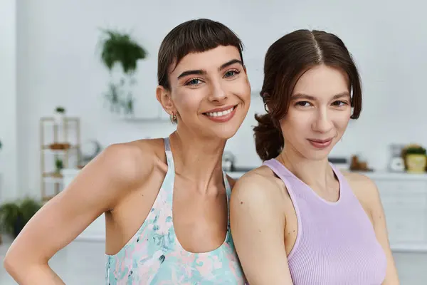 Two young women in sportswear smile at the camera while working out in a modern apartment. — Stock Photo