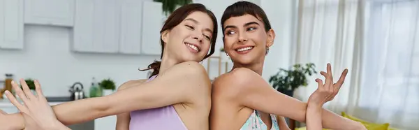 Duas jovens sorridentes em roupas esportivas fazem um exercício dinâmico juntas, de um lado para o outro, em seu apartamento moderno. — Fotografia de Stock
