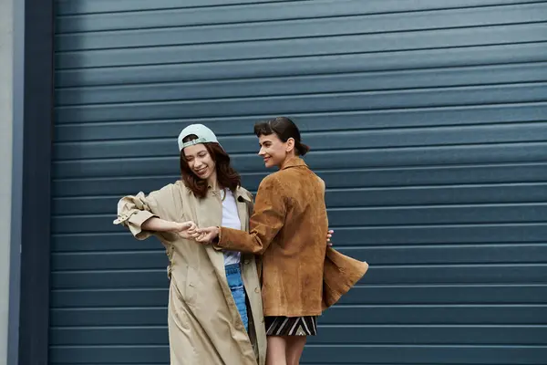 Two young women in trendy attire walk together in front of a blue garage door. — Stock Photo