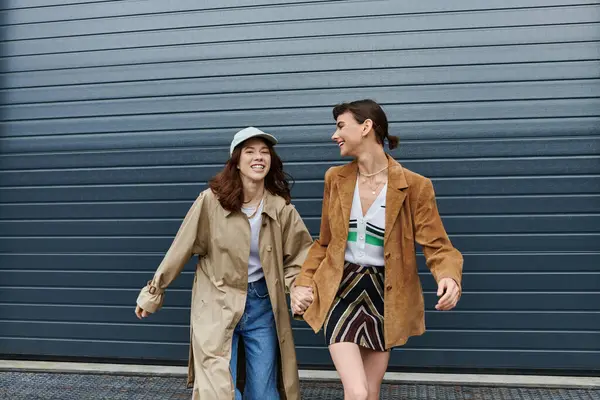 Two stylish young women walk hand-in-hand, laughing and enjoying a sunny day outdoors. — Stock Photo