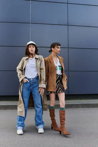 Two young women in trendy outfits stand together on a city street, sharing a moment. — Stock Photo