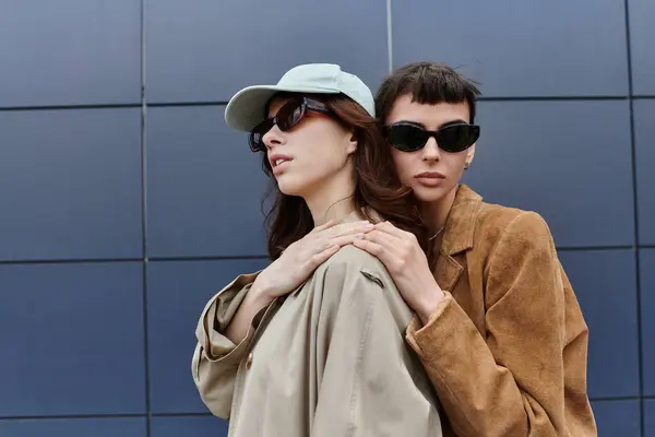 Due giovani donne in abiti alla moda stanno vicine in un ambiente urbano, una con una mano sulle spalle. — Foto stock