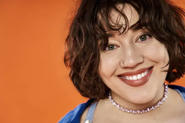 A woman smiles brightly in front of a vibrant orange background. — Stock Photo