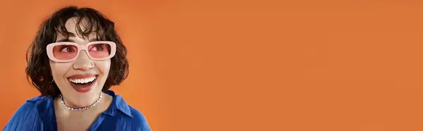 A woman in pink sunglasses smiles brightly against a vibrant orange backdrop. — Stock Photo