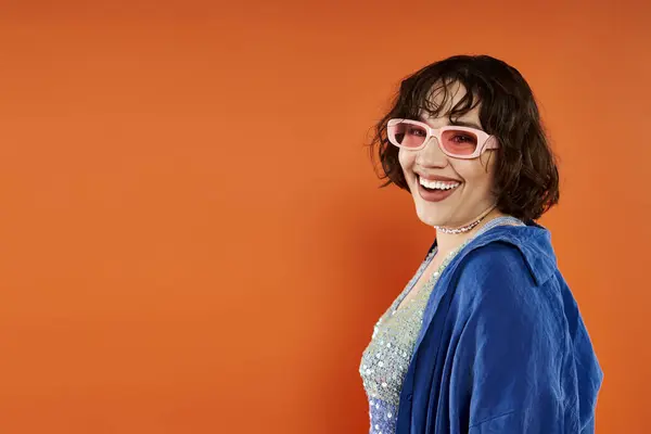 A woman smiles brightly while wearing pink sunglasses and a blue jacket. — Stock Photo