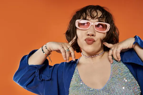 A woman in vibrant attire strikes a playful pose against a bright orange backdrop. — Stock Photo