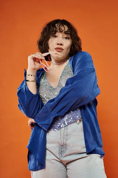A woman in a blue shirt and sequined top poses confidently against a vibrant orange backdrop. — Stock Photo