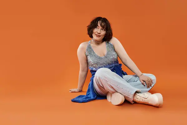 Woman in a sparkly top smiles while sitting on an orange backdrop. — Stock Photo