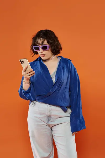 A woman in a blue shirt and sunglasses looks surprised at her phone. — Stock Photo