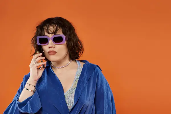 Femme en chemise bleue, soutien-gorge coloré, parle au téléphone sur fond orange — Photo de stock