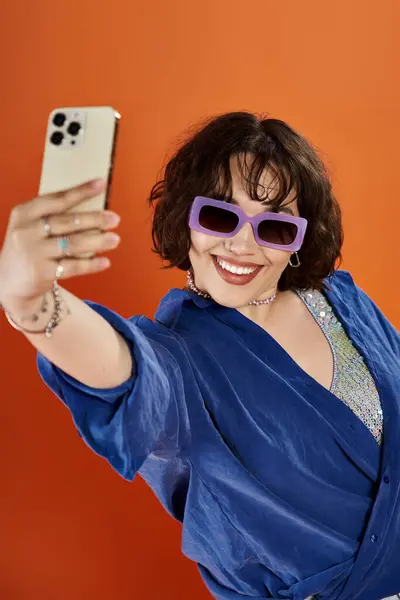 A woman in a blue shirt takes a selfie, smiling broadly in vibrant sunglasses. — Stock Photo