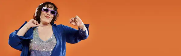 A woman in a blue jacket and sparkly top dances against a vibrant orange backdrop. — Stock Photo