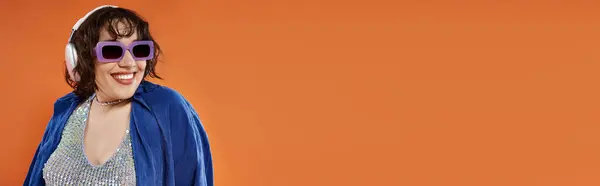 A woman in blue clothing smiles against an orange background. — Stock Photo