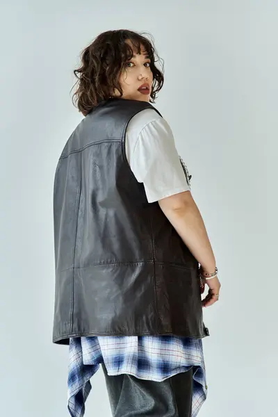 Una donna con i capelli scuri si guarda alle spalle, indossando un lungo gilet di pelle e una camicia a quadri. — Foto stock