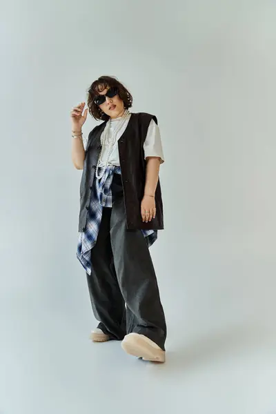 A woman poses confidently, wearing a black vest over a white t-shirt and wide-leg pants. — Stock Photo
