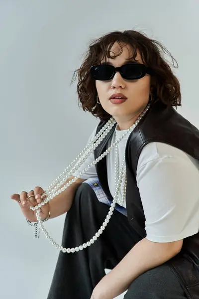 A woman in sunglasses and a black vest sits with a long pearl necklace. — Stock Photo