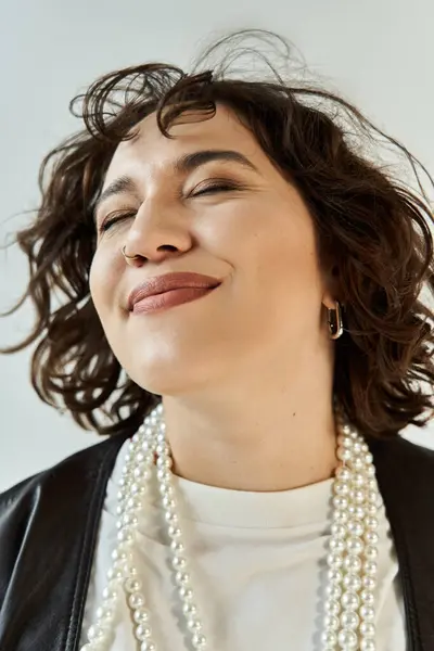 Curly-haired woman in white shirt and black jacket, adorned with pearls — Stock Photo