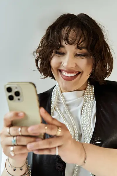 Uma mulher usando um colar de pérolas e um casaco preto sorri enquanto olha para o telefone. — Fotografia de Stock