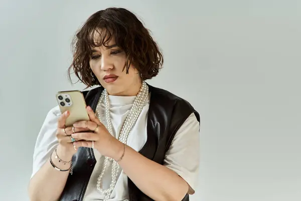 A woman in a vibrant vest looks intently at her phone. — Stock Photo
