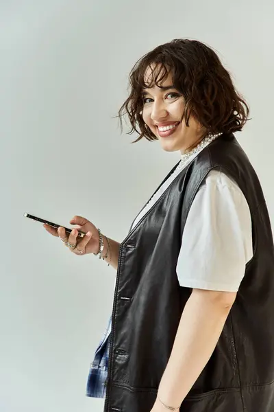 A woman in a leather vest looks at her phone and smiles. — Stock Photo