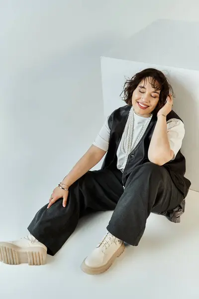 A woman in a black vest and white shirt smiles brightly, sitting on a white background. — Stock Photo