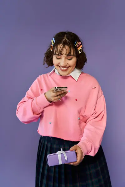 A woman smiles brightly while looking at her phone, holding a gift in her other hand. — Stock Photo