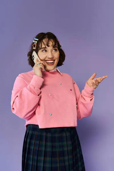 A young woman in pink and plaid smiles as she talks on the phone. — Stock Photo