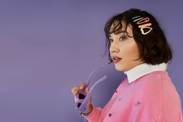 A young woman in a pink sweater gazes off-camera, holding purple sunglasses. — Stock Photo