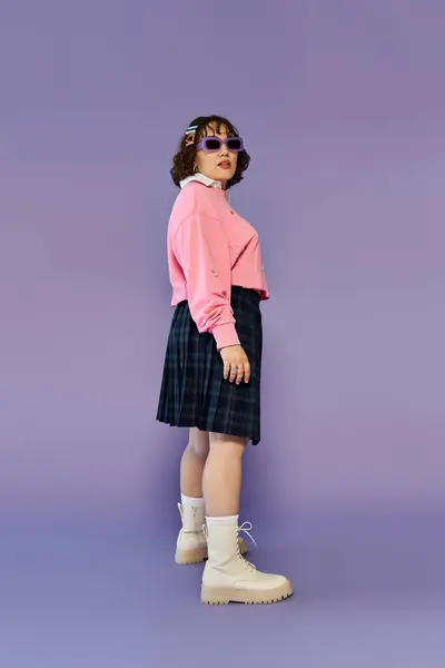 Una donna posa in un maglione rosa e gonna a quadri. — Foto stock