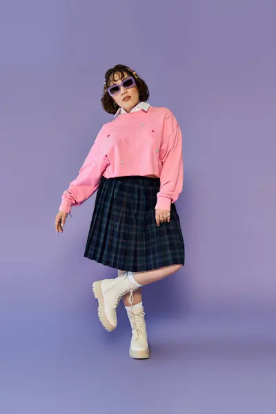 A woman in a pink sweater and plaid skirt poses in front of a lavender background. — Stock Photo