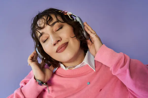 A woman in a pink sweater, eyes closed, listens to music with headphones on, lost in the sound. — Stock Photo