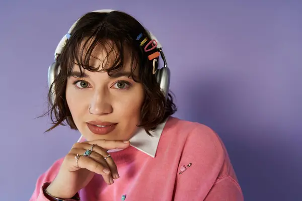 A woman with headphones and colorful hair clips rests her chin on her hand, lost in thought. — Stock Photo