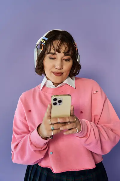 Young woman in pink sweater and headphones, using phone against purple backdrop — Stock Photo