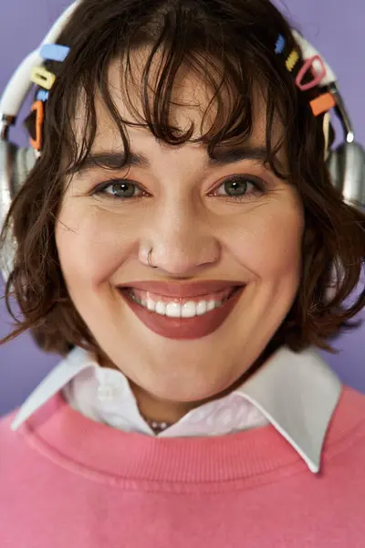 Woman in pink sweater smiles with headphones on, against purple background — Stock Photo
