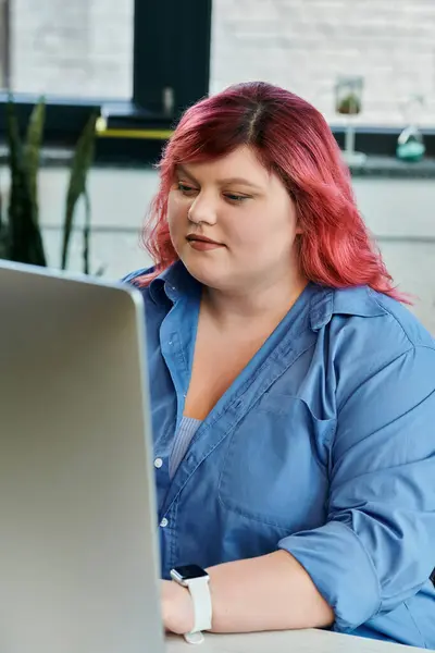 A plus size woman with pink hair works intently on a laptop. — Stock Photo