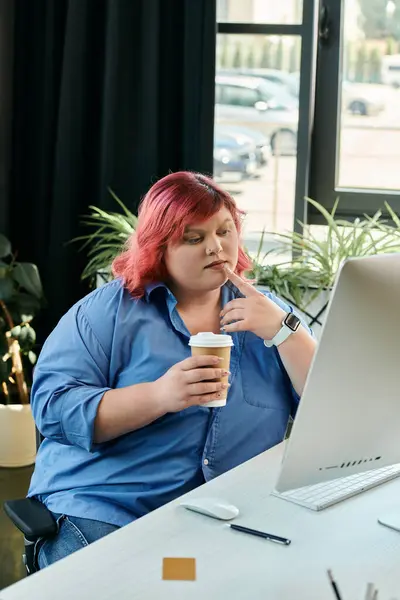 Une femme d'affaires de taille plus avec les cheveux roses s'assoit à son bureau, contemplant son travail tout en tenant une tasse de café. — Photo de stock