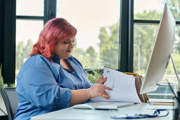 A plus size businesswoman with pink hair sits at a desk reviewing documents. — Stock Photo