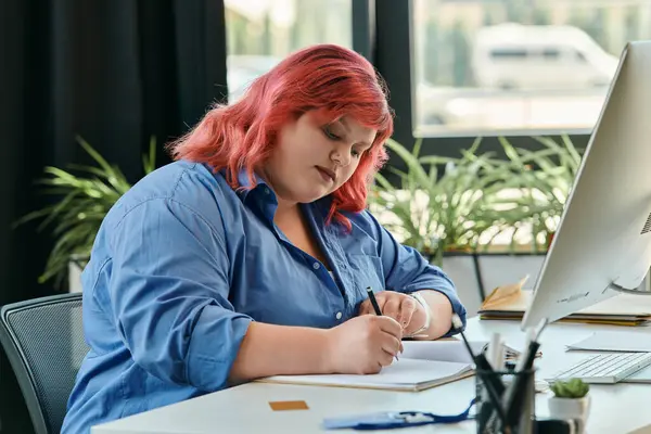 A plus size businesswoman with pink hair sits at a desk, focused on writing in a notebook. — Stock Photo